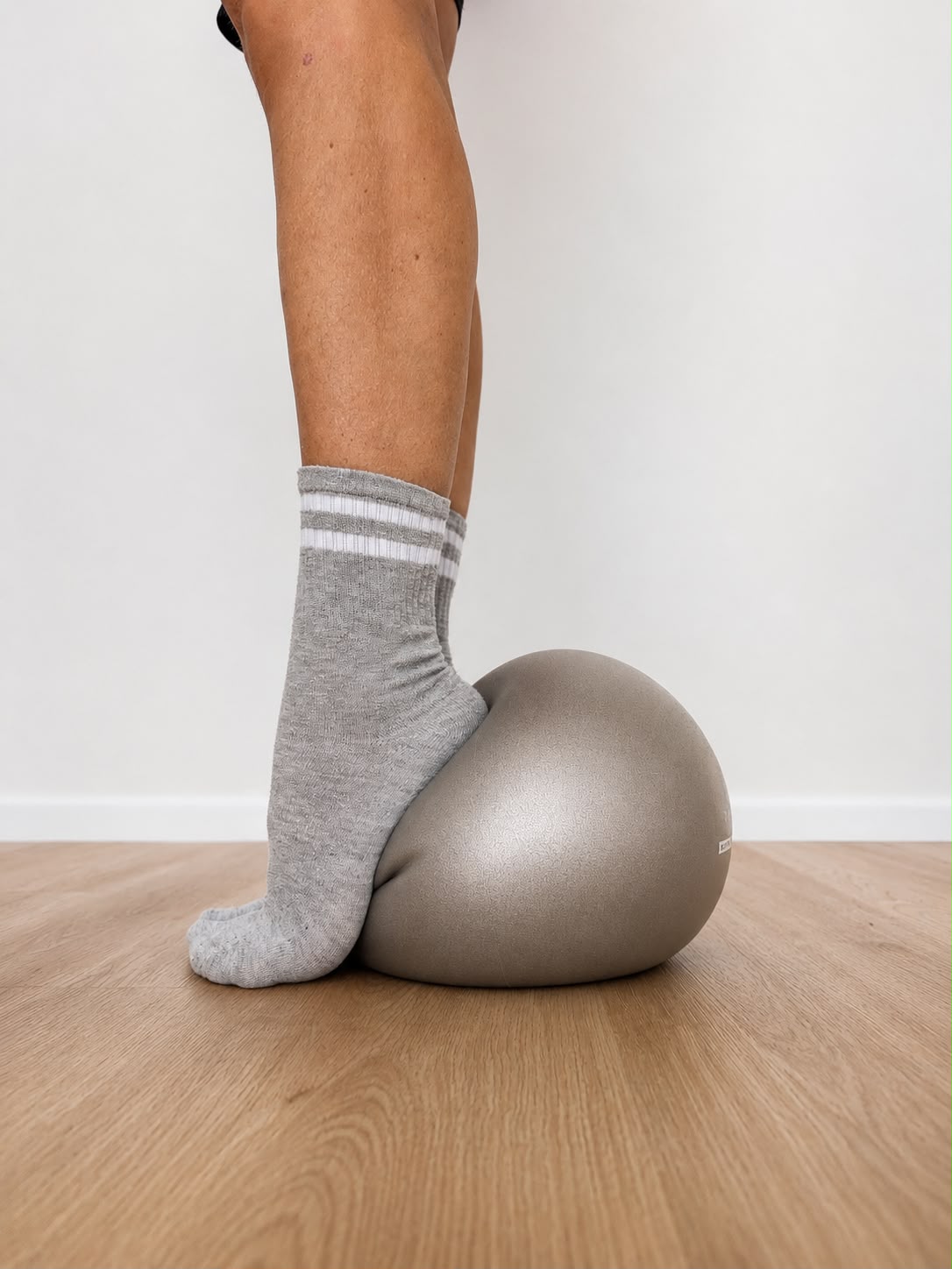 Palla da pilates e gambe con calze grigie su pavimento in legno nello studio Feel Good